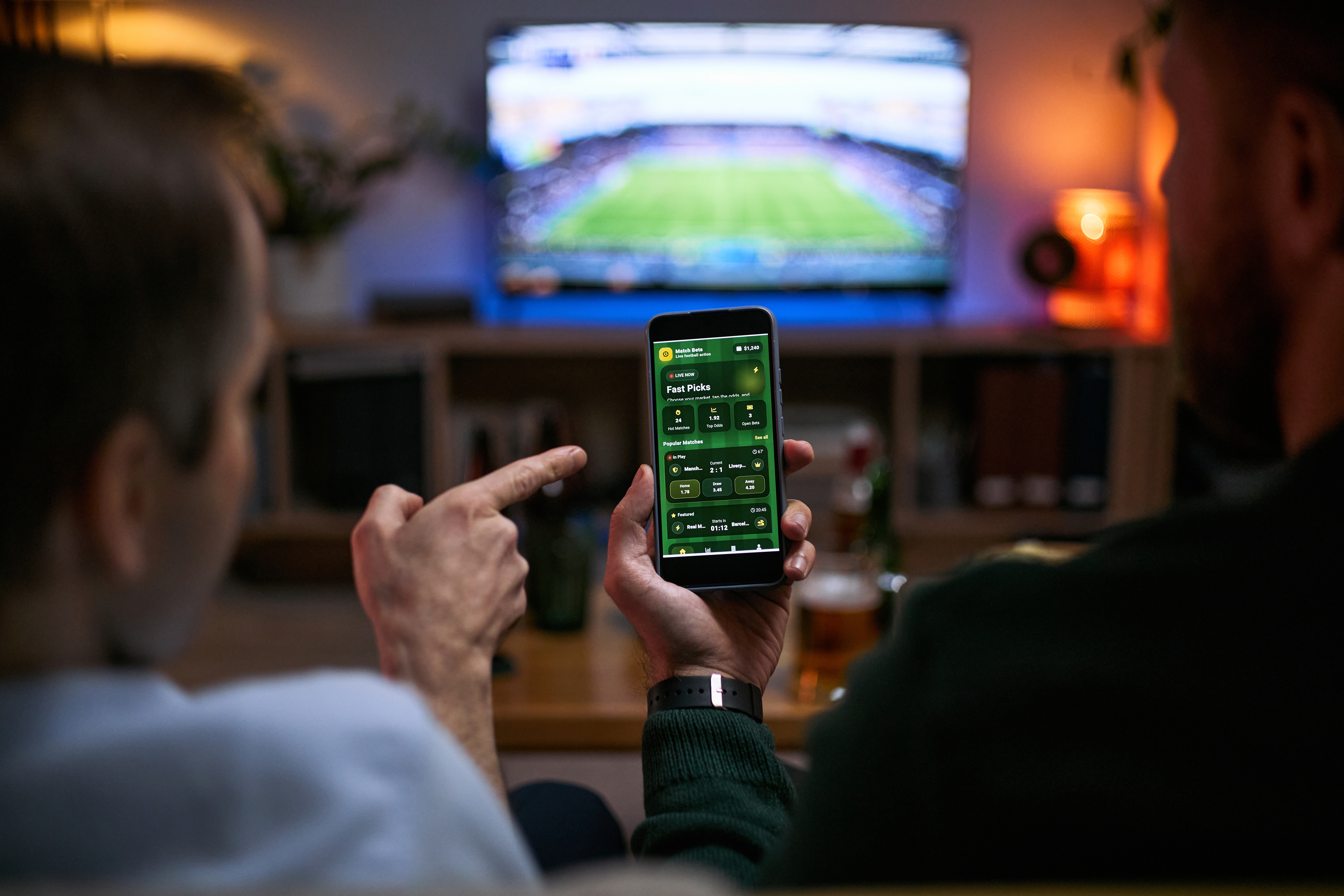 Two people looking and pointing and phone while watching football