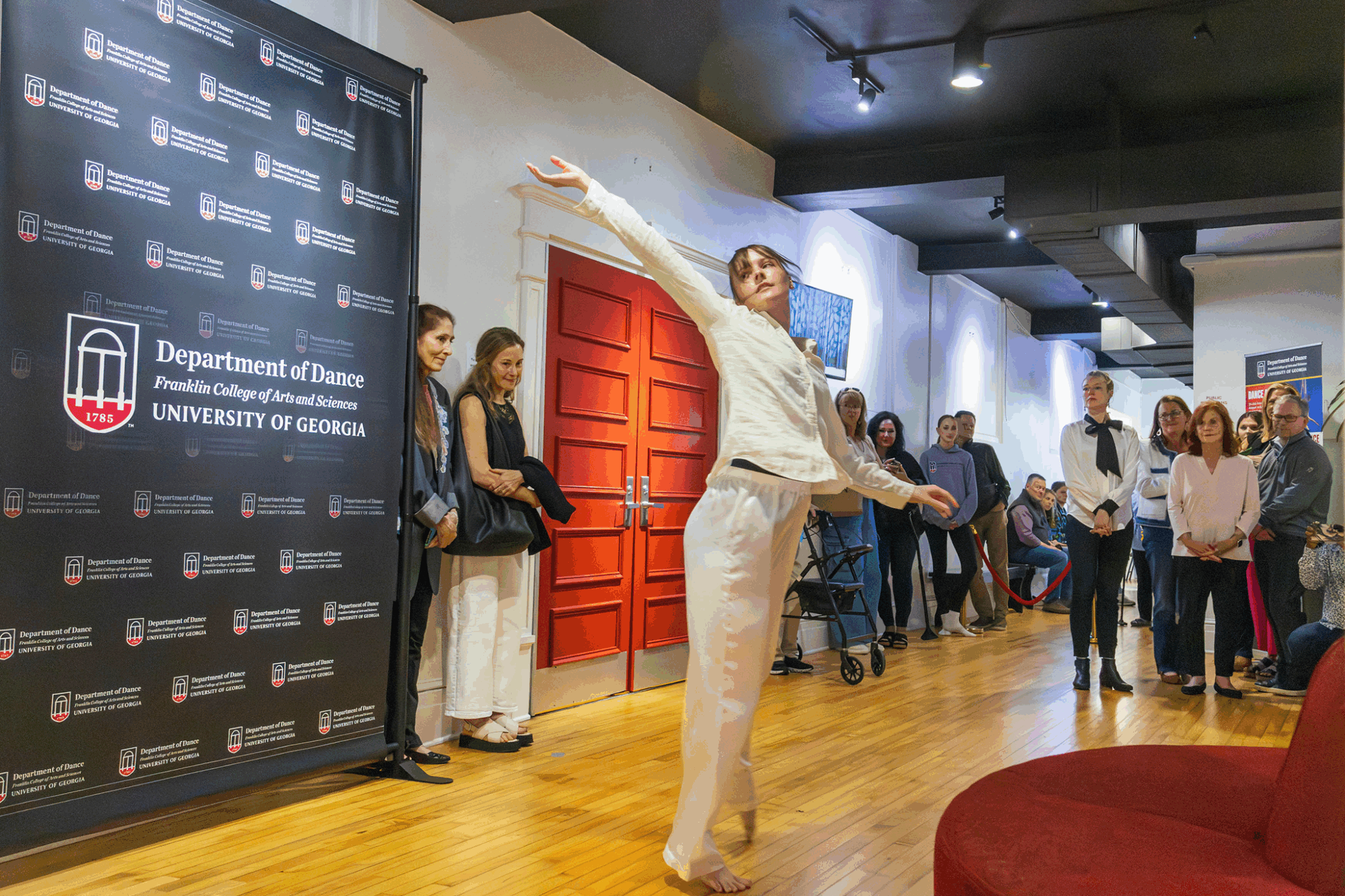 woman dances in room, people and banner in background.