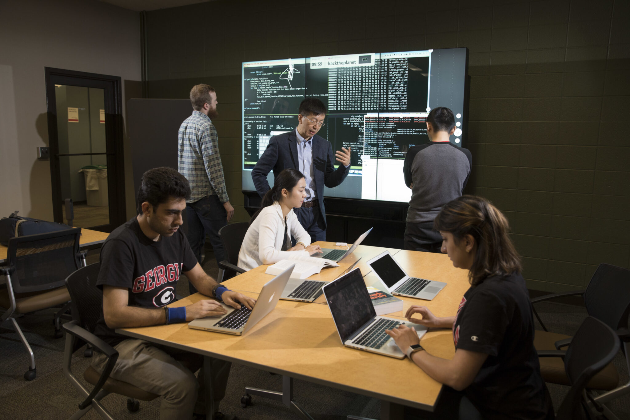 photo of six people in a room with laptop and projection screen, table