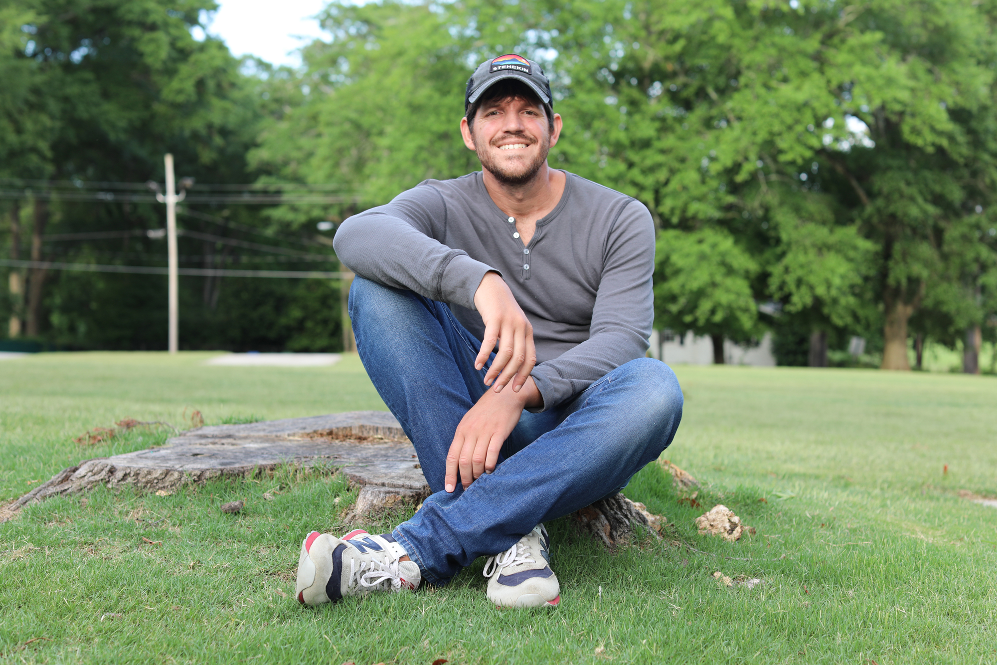 photo. of man sitting outside on tree stump