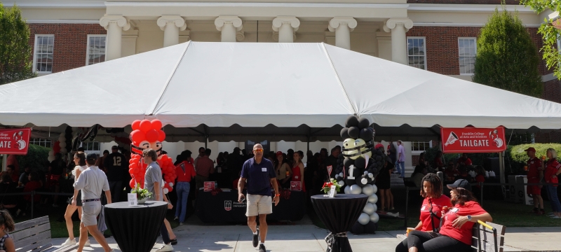 wide photo of tent event with people, building, blue sky