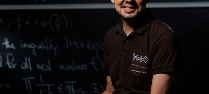 photo of man, chalkboard with letters and numerals in background