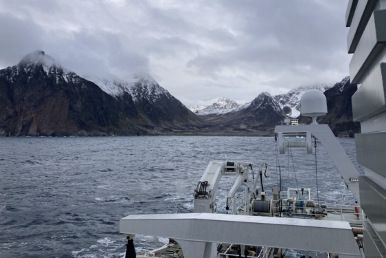 photo of shoreline mountain with clouds, sea and ship in foreground