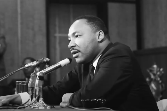 black and white photo of man seated at table with microphone